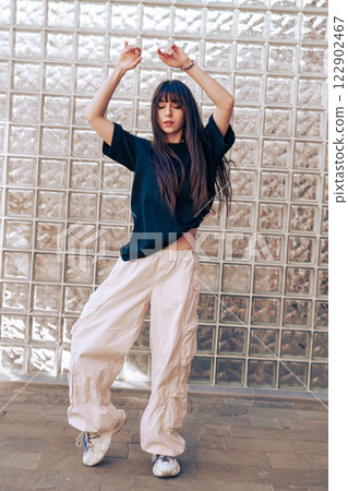 Dancer performing expressive movements in urban setting with glass brick background during daylight 122902467