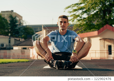 Young man exercising in a sporty outfit on an athletic track during late afternoon Young man exercising in a sporty outfit on an athletic track during late afternoon 122902476