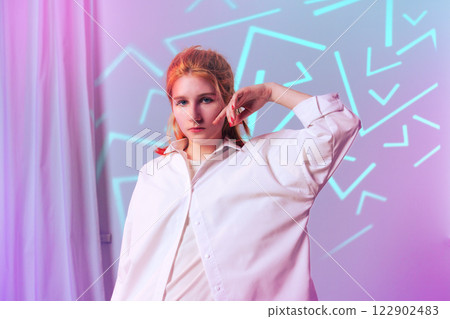 Young woman poses confidently in oversized shirt against colorful geometric backdrop at a creative studio Young woman poses confidently in oversized shirt against colorful geometric backdrop at a creative studio 122902483