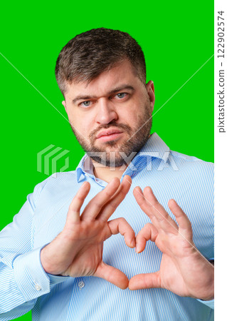 A man forming a heart shape with his hands against a vibrant green background A man forming a heart shape with his hands against a vibrant green background 122902574