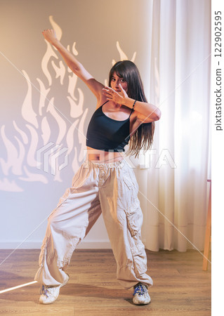 Dancer showcases impressive moves in casual attire with playful shadows in studio setting Dancer showcases impressive moves in casual attire with playful shadows in studio setting 122902595