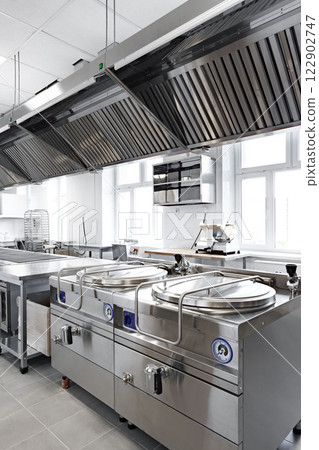 Modern commercial kitchen equipped with stainless steel appliances and ventilation system for culinary operations 122902747