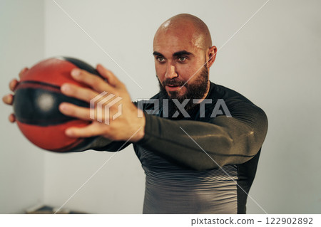 Fitness enthusiast practicing strength training with a medicine ball in a gym setting Fitness enthusiast practicing strength training with a medicine ball in a gym setting 122902892