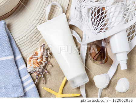 Sunscreen cream tube, sunglasses, towel, starfishes and seashells on a sand, cosmetic mockup 122902956