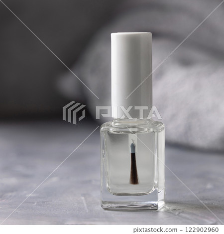 Clear glass bottle with white blank brush cap near grey towel on grey closeup. Nail product mockup Clear glass bottle with white blank brush cap near grey towel on grey closeup. Nail product mockup 122902960