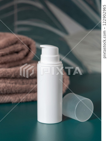 White cream bottle near brown towels in dark green tropical bathroom close up, cosmetic mockup White cream bottle near brown towels in dark green tropical bathroom close up, cosmetic mockup 122902965