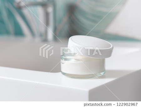 Opened cream jar with blank lid on washbasin in green tropical bathroom close up, cosmetic mockup 122902967