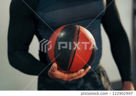 Smiling athlete holding a basketball indoors during a training session in a modern gym Smiling athlete holding a basketball indoors during a training session in a modern gym 122902997