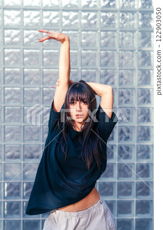 Young dancer performing expressive movement in front of glass brick wall during a creative dance session 122903050