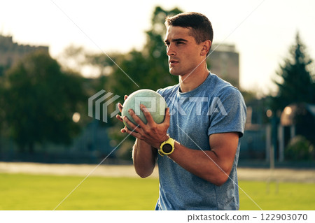 Athlete prepares for shot put competition at a sunny outdoor track and field facility 122903070
