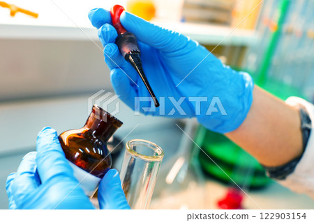 Lab technician conducts an experiment using pipette and glass vial in a laboratory setting during daytime 122903154