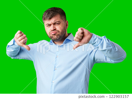 Man expressing disapproval with thumbs down gesture against a bright green background Man expressing disapproval with thumbs down gesture against a bright green background 122903157