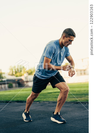 Runner checking smartwatch for pace during training session on a track field in the afternoon sun 122903163