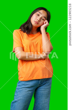 Young woman in orange shirt poses thoughtfully against a bright green background in a studio setting Young woman in orange shirt poses thoughtfully against a bright green background in a studio setting 122903218