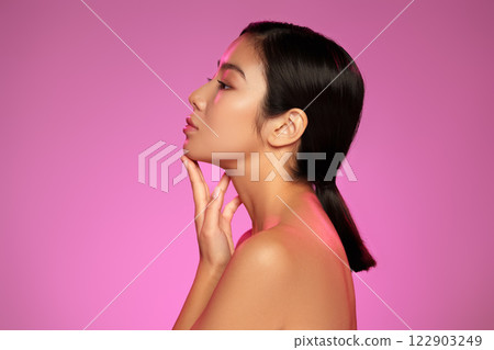 Elegant profile of a young woman with sleek hair posed against a vibrant pink background showcasing beauty and grace 122903249