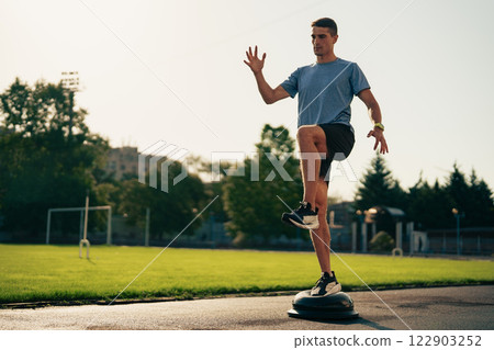 Young man practicing balance on a stability disc in a park during daylight hours 122903252