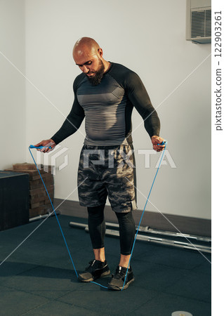 Man skipping rope indoors during workout session at gym with fitness equipment 122903261