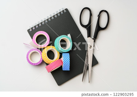 Crafting essentials on a workspace featuring colorful tape and scissors beside a notepad 122903295