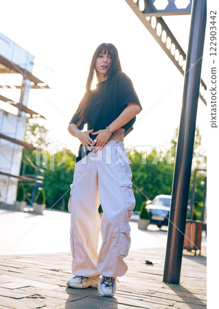 Fashionable young woman poses confidently in urban setting during late afternoon light Fashionable young woman poses confidently in urban setting during late afternoon light 122903442