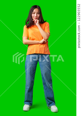 Young woman standing confidently with a thoughtful expression in bright orange shirt and jeans 122903552