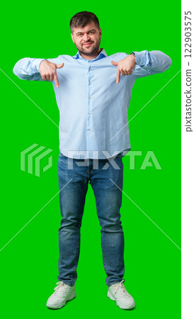 Man in a blue striped shirt and jeans gesturing downward against a bright green background Man in a blue striped shirt and jeans gesturing downward against a bright green background 122903575
