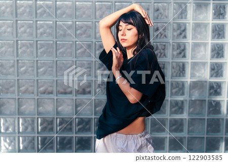Woman gracefully dancing in a minimalist space with glass block wall in the background during a sunny afternoon 122903585