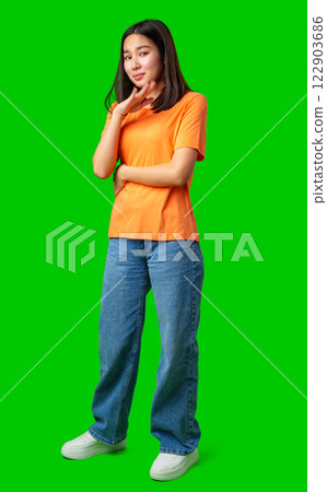 Young woman in orange shirt poses confidently with green background in a creative indoor setting Young woman in orange shirt poses confidently with green background in a creative indoor setting 122903686