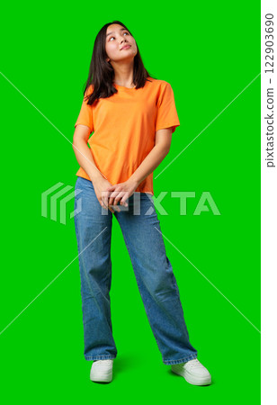 Woman in casual outfit poses with a thoughtful expression in front of a bright green background 122903690