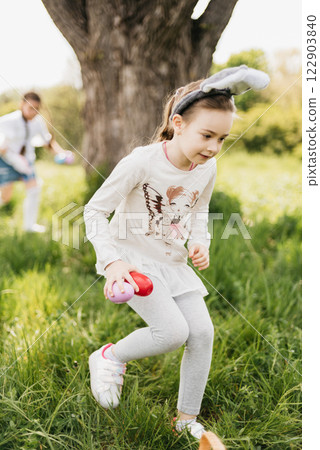 Easter egg hunt. Group Of Children Wearing Bunny Ears Running To Pick Up colorful Egg On Easter Egg Hunt In Garden. Easter tradition. Laughing children in park with basket spring concept 122903840