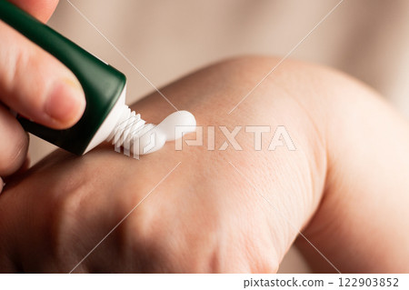 Woman applying hand cream on hands. Close up image of white cream. Squeeze cream out of tube. Soft hands and skincare concept. Woman applying hand cream on hands. Close up image of white cream. Squeeze cream out of tube. Soft hands and skincare concept. 122903852