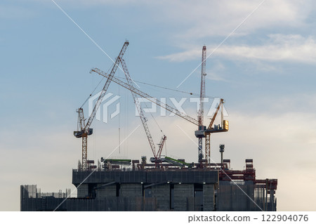Close-up industrial big cranes working on construction site to build modern tall buildings on evening, growth in the city 122904076