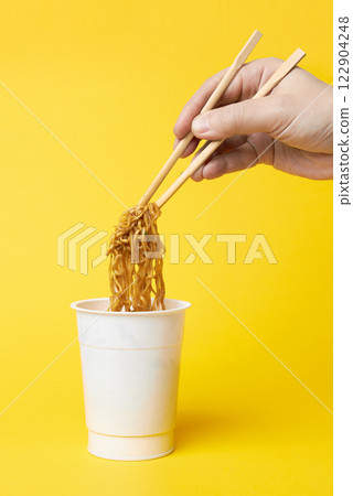 Instant noodles and hand with chopsticks in a yellow 122904248