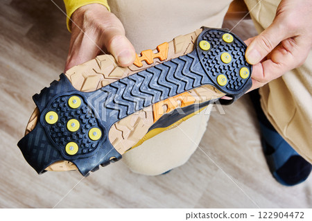 Close-up of yellow hiking boot fitted with black rubber anti slip crampons, featuring yellow metal spikes for traction on icy surfaces. 122904472