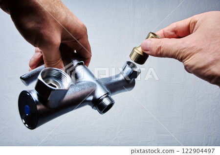 Hands attach brass eccentric reducer to plumbing fixture of . bathroom mixer tap with threaded connectors. Hands attach brass eccentric reducer to plumbing fixture of . bathroom mixer tap with threaded connectors. 122904497