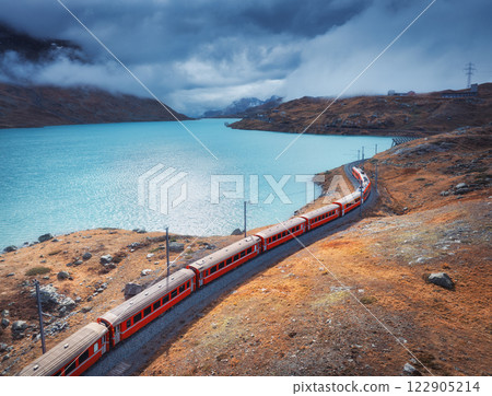 Aerial view of red train near alpine mountain lake and cloudy sky Aerial view of red train near alpine mountain lake and cloudy sky 122905214