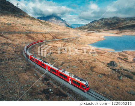Aerial view of red train near alpine mountain lake and cloudy sky 122905215