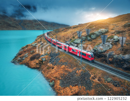Aerial view of red train near alpine mountain lake and cloudy sky 122905232