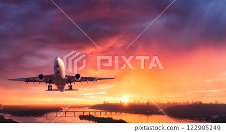 Airplane is flying in colorful sky over city at sunset. Aerial 122905249