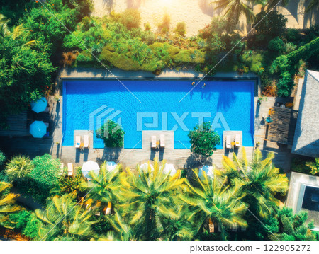 Aerial view of swimming pool, sunbeds and umbrellas, green palms 122905272