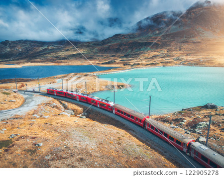 Aerial view of red train near alpine mountain lake and cloudy sky Aerial view of red train near alpine mountain lake and cloudy sky 122905278