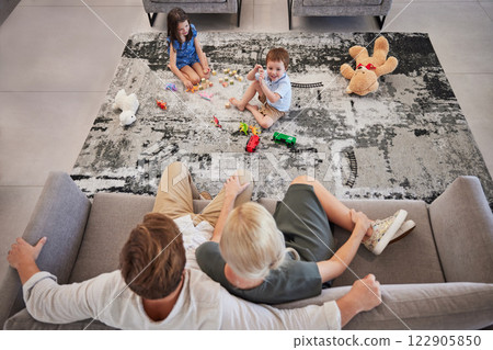 Family, children and living room with a girl and boy playing on the floor of their home while their parents relax on the sofa. Toy, fun and game with a brother and sister bonding with mom and dad 122905850