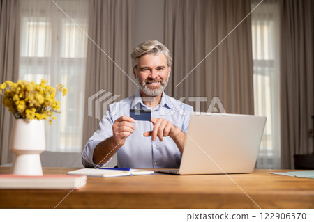 Gray-haired mature man sitting at the laptop and making notes while working Gray-haired mature man sitting at the laptop and making notes while working 122906370