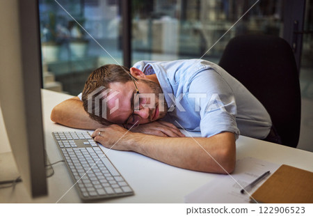 Burnout, tired and sleep with a business man sleeping on his desk while working on a computer at a desk in his office. Mental health, problem and exhausted with a young male employee at work at night 122906523