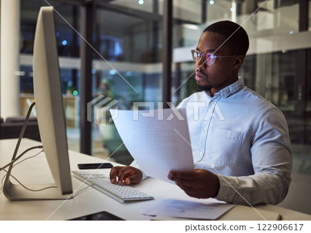 Contract, documents and data with a businessman working at night on a computer in an office. Research, reading and information with a black male employee at work at a desk on an international company Contract, documents and data with a businessman working at night on a computer in an office. Research, reading and information with a black male employee at work at a desk on an international company 122906617