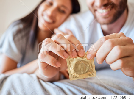 Condom, couple and sex with the hands of a man opening protection for sexual intercourse in bed with a partner. Happy, love and safe with a woman and her boyfriend using contraceptive in the bedroom 122906962