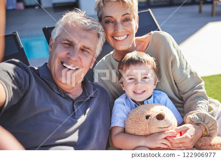 Grandparents, boy and backyard selfie in home on lawn chairs on grass sharing love, energy and bonding. Portrait of retired happy man, woman and kid with teddy, caring and enjoying time together. 122906977