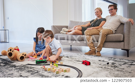 Happy family, bonding and children playing in living room, relax and cheerful in their home together. Loving parents smile and enjoy parenthood, watching kids play on a floor while resting on couch 122907503