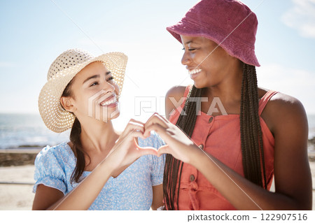 Happy interracial friends, smile and heart hand sign for love, beach and outdoor freedom together on summer vacation. Women couple in loving shape gesture for friendship happiness and joy on holiday Happy interracial friends, smile and heart hand sign for love, beach and outdoor freedom together on summer vacation. Women couple in loving shape gesture for friendship happiness and joy on holiday 122907516