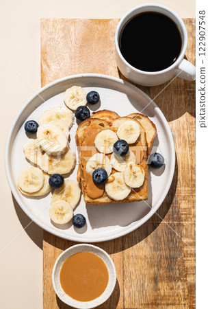 Peanut butter toast with banana and blueberry on a wooden board with a cup of freshly brewed coffee Peanut butter toast with banana and blueberry on a wooden board with a cup of freshly brewed coffee 122907548