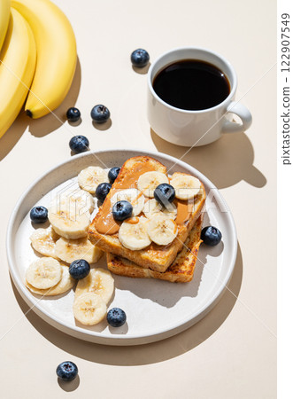 Peanut butter toast with banana and blueberry on a plate on a beige background with a cup of coffee Peanut butter toast with banana and blueberry on a plate on a beige background with a cup of coffee 122907549